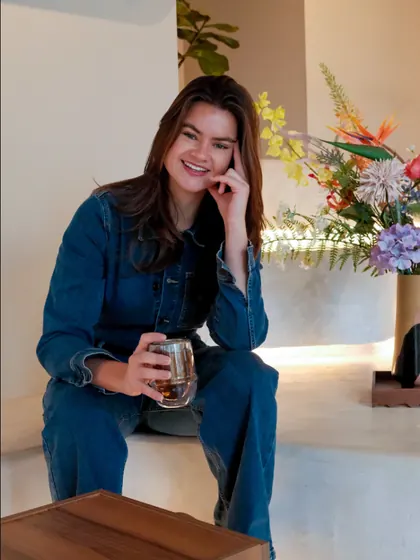 Someone sitting on the built-in bench at nous, holding a glass cup, with flowers behind.
