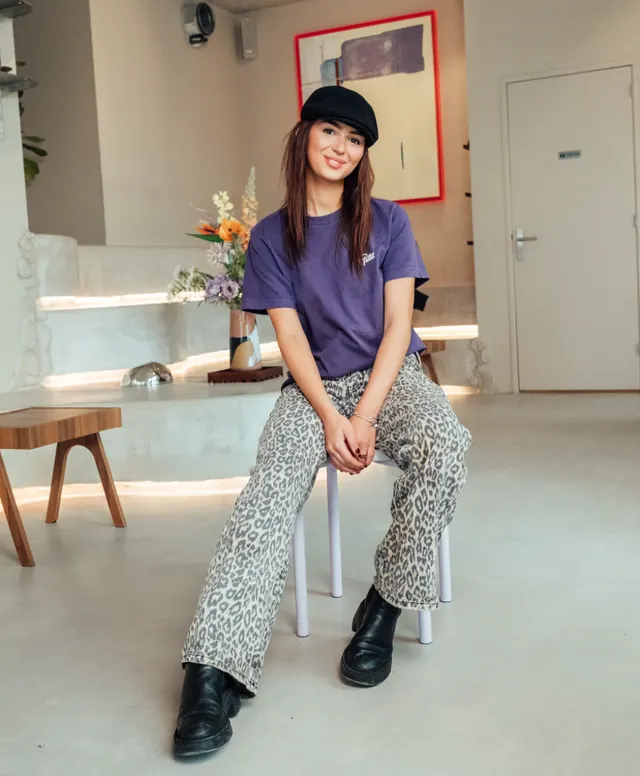 Inside nous Noord: someone sitting on a lilac stool in a warm micro-cement room with a lit bench and flowers.