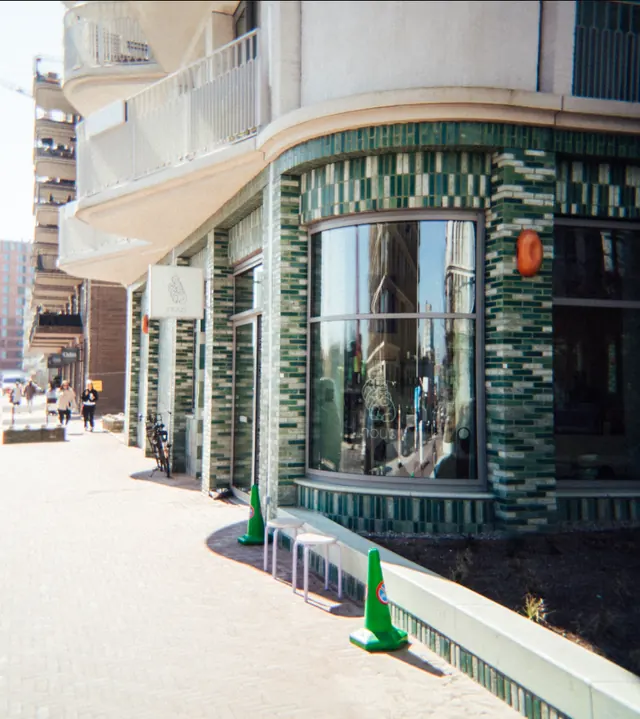 The corner of nous on the Haarlemmerplein in Amsterdam, clad in green glazed brick with the hanging nous sign.